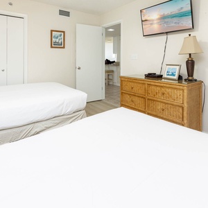 Guest bedroom featuring two double beds, a wooden dresser, a TV mounted on the wall, and a door leading to the living area