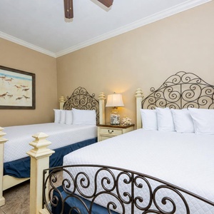 This guest bedroom features two elegant full beds with decorative iron headboards and a cozy lamp, perfect for restful nights
