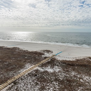 Balcony beach view with soft white sand and gentle waves, framed by a serene sky dotted with clouds