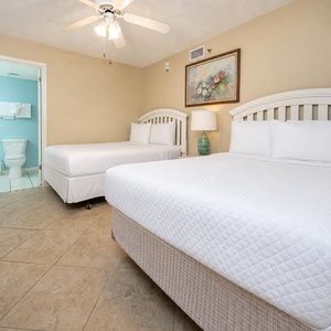 Cozy guest bedroom featuring two double beds, a decorative lamp, and an adjoining bathroom with a soothing blue accent wall
