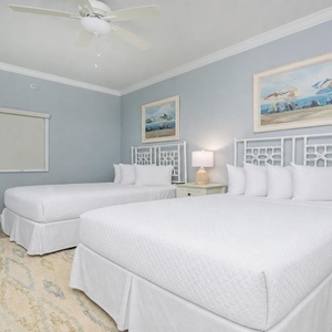 Serene guest bedroom featuring two queen beds, soft linens, and coastal artwork