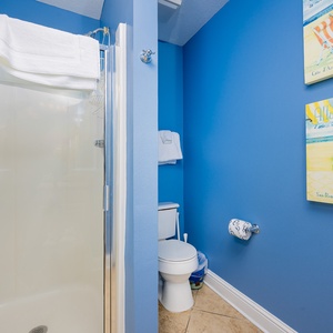 This guest bathroom features a vibrant blue wall, a sleek shower, and cheerful beach-themed artwork for a refreshing retreat