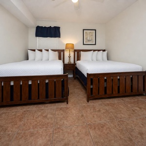 Bright and inviting guest bedroom featuring two comfortable double beds, a stylish lamp, and warm wooden accents