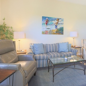 The living area features a striped sofa with plush cushions, a sleek glass coffee table, and vibrant beach-themed artwork