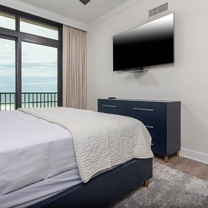 This bedroom features a cozy king bed, a mounted TV, and stunning beachfront views through large windows