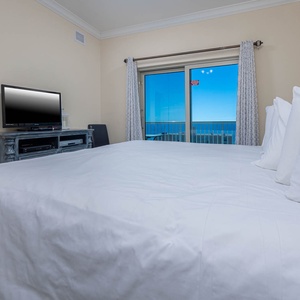 This bedroom features a cozy bed, a TV for entertainment, and a stunning view of the beach through large sliding doors
