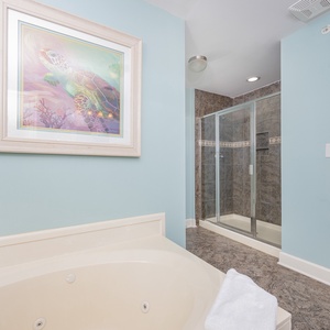 Relax in this serene master bath featuring a jetted tub, walk-in shower, and soothing blue walls adorned with beach art