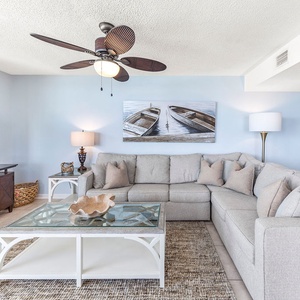 The inviting living area features a large sectional sofa adorned with decorative pillows, a sleek TV, and coastal artwork