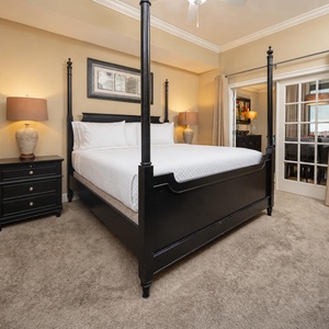 The master bedroom features a four-poster king bed, soft beige walls, and a warm lamp, creating a relaxing retreat