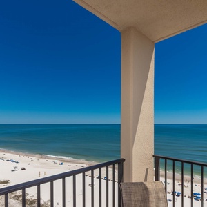 The balcony offers a breathtaking view of the beach with vibrant blue umbrellas dotting the white sand below