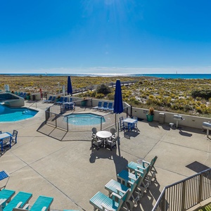 Relax by the pool area surrounded by lounge chairs, with a view of the gulf and lush greenery in the distance