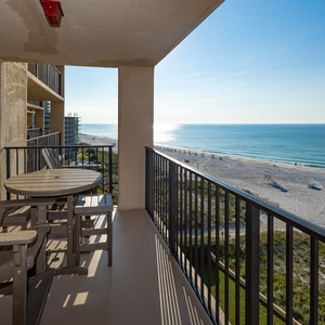 Balcony with a round table and chairs offers a serene view of the beach and calm waters stretching to the horizon