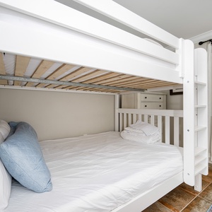 Queen over queen bunk bed with soft linens and a blue accent pillow, perfect for a restful sleep in a charming guest room