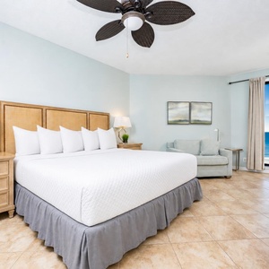 The master bedroom features a king-sized bed, a cozy seating area, and stunning beachfront views through large windows