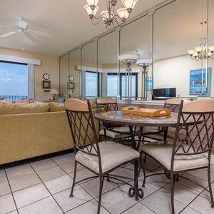 Cozy seating area features a plush sofa and a round dining table, with expansive windows offering a view of the gulf