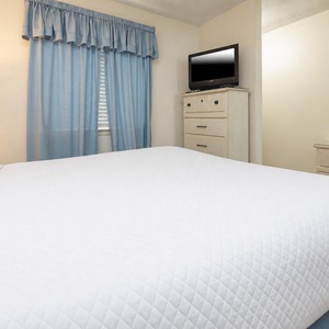 The bedroom features soft blue curtains, a cozy queen bed, and a TV for your entertainment