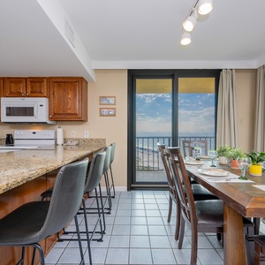 The kitchen features wooden cabinetry, a granite countertop, and a dining area with a view of the beach through large windows
