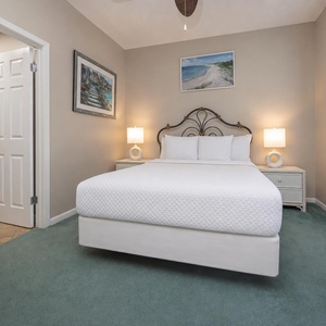 Serene guest bedroom features a plush queen bed, soft green carpet, and warm lighting from bedside lamps