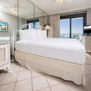 Master bedroom featuring a plush king bed, elegant decor, and a view of the balcony with seating overlooking the beach