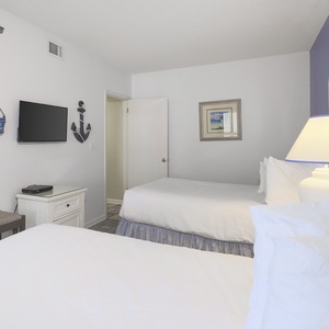 Cozy guest bedroom featuring two double beds, a wall-mounted TV, and nautical decor for a relaxing beach getaway
