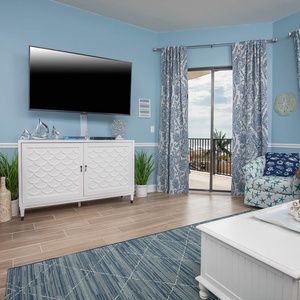 The living area features a cozy sofa with queen sleeper, blue accents, and large windows that invite in the beach views