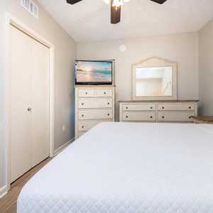 Relax in this comfortable bedroom featuring a large king bed, dresser, TV, and natural light from the nearby window