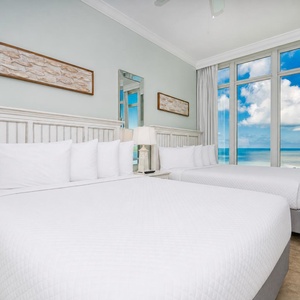 Relax in this guest bedroom with two queen beds, large windows showcasing beautiful beach views, and coastal accents
