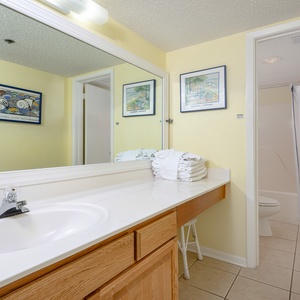 Brightly colored master bath featuring a spacious vanity, neatly stacked towels, and a tub/shower combo behind a curtain