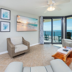 Cozy living area featuring a large TV and stunning views of the beach through expansive glass doors leading to the balcony