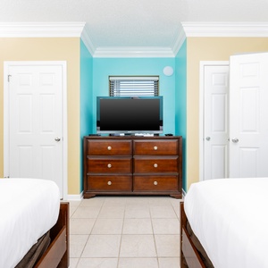This guest bedroom features two queen beds, a dresser with a flat-screen TV, and colorful walls that create a cheerful vibe
