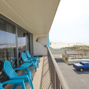 The balcony features bright blue chairs and stunning views of the beach, perfect for relaxing and enjoying the scenery