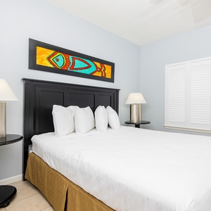Brightly decorated guest bedroom featuring a plush queen bed with decorative pillows, stylish lamps, and vibrant wall art