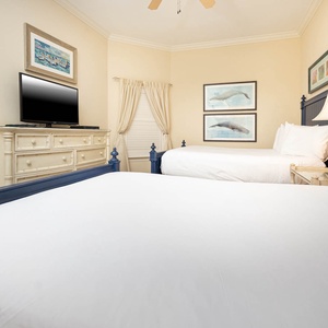 This guest bedroom features two queen beds, a TV for entertainment, and charming coastal artwork on the walls