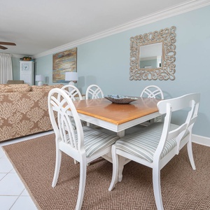 Dining area features a wooden table with striped chairs, complemented by a coastal decor and a view of the beach
