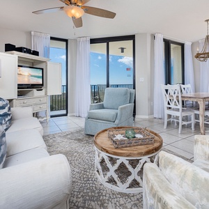 Cozy living area features a plush sofa with decorative pillows, armchairs, and dining table, all with expansive beach views