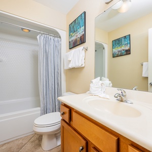 The bathroom features a tub-shower combo, bright lighting, and decorative artwork for a refreshing ambiance