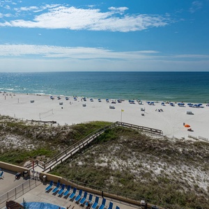 The balcony view showcases a serene beach with white sand, colorful umbrellas, and a clear blue sky above the tranquil water