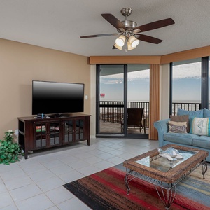 Cozy living area features a blue loveseat with beach pillows, a glass coffee table, and sliding doors leading to a balcony