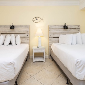 Two cozy double beds with white linens and wooden headboards create a welcoming atmosphere in this vibrant guest room