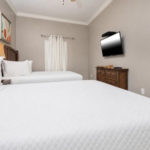 Rest comfortably in this guest bedroom featuring two queen beds, a TV, and soft lighting for a relaxing vibe