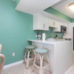 This kitchen features bright teal walls, sleek white cabinetry, and a convenient breakfast bar with stylish stools