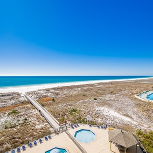 Expansive beachfront view showcases the sparkling gulf and white sand, with an inviting pool and lounging areas below