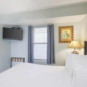 The bedroom features a comfortable bed, a mounted TV, and charming artwork, perfect for a relaxing stay