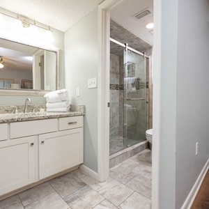 The master bathroom features a granite countertop vanity, a large mirror, and a walk-in shower with modern glass doors