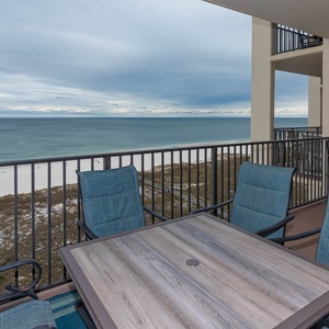 Balcony seating with a table offers a serene view of the tranquil gulf and white sand, perfect for relaxation