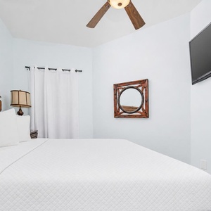 This cozy guest bedroom features a king-sized bed, a mounted TV, and calming blue walls, perfect for relaxation