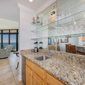Kitchen wet bar area with a beachfront view, ice-maker, blender, and elegant glassware display for entertaining guests