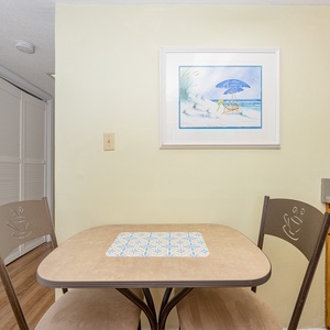 This cozy dining area features a small table, cheerful artwork, and warm wood cabinetry, perfect for shared meals