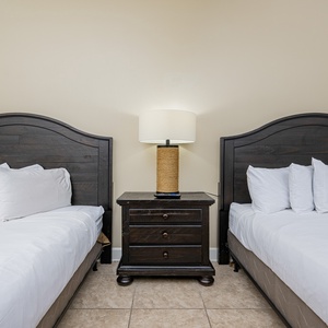 Rest in this guest bedroom featuring two queen beds, a stylish lamp, and relaxing tones