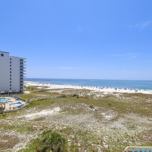 Expansive view of the beach with white sand, inviting turquoise waters, and the jetties at the pass in the distance